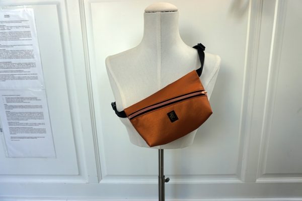 kupferfarbene Kunstlederhandtasche im Stil einer Bauchtasche.