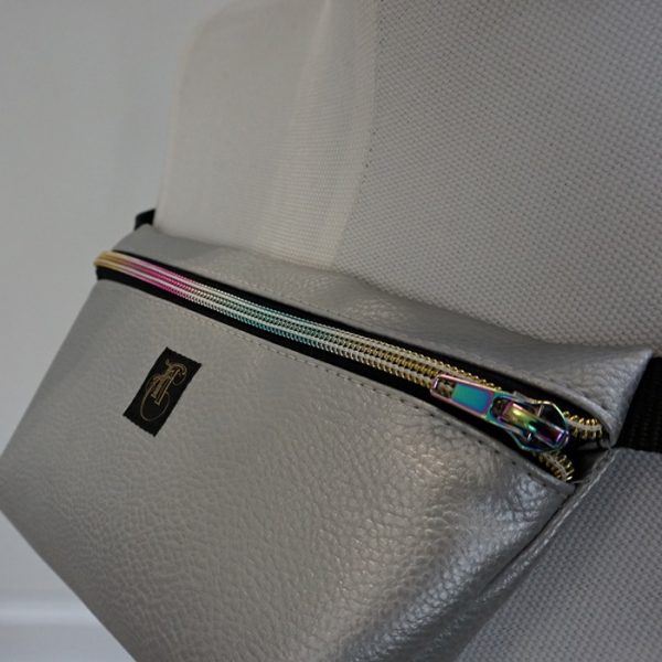 Detailaufnahme; silberfarbene Kunstlederhandtasche im Stil einer Bauchtasche.